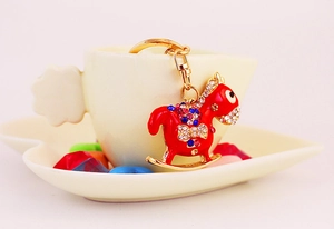 Detail of red rocking horse keychain with colorful rhinestones on a coffee cup