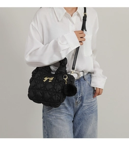 Detail of black quilted crossbody bag with gold bow and soft pompom charm on white shirt