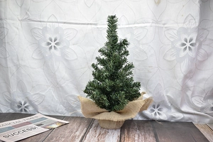 Miniature green Christmas tree with a rustic burlap base on a warm wooden desk