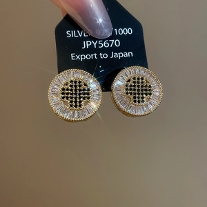 Close-up of gold plated round earrings with clear zircon inlay and black cross pattern