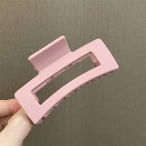Primer plano de una pinza para el cabello cuadrada rosa mate sostenida sobre fondo gris