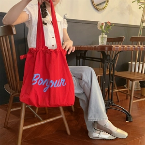 Close-up of a red canvas tote bag with blue Bonjour print in a cafe setting