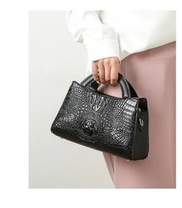 Crocodile pattern black handbag with gold V buckle shown being carried by a model