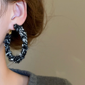 Gros plan d'une grande créole dorée enveloppée de tissu en tweed noir et blanc sur modèle
