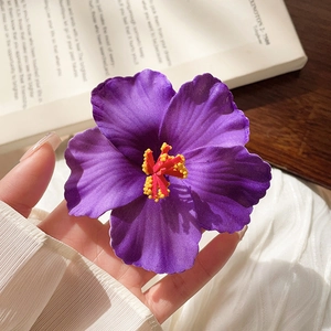 Close-up of a purple fabric frangipani flower hair clip with realistic yellow stamen detail