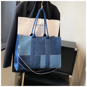 Close-up of large denim tote bag featuring blue patchwork design and wide shoulder strap