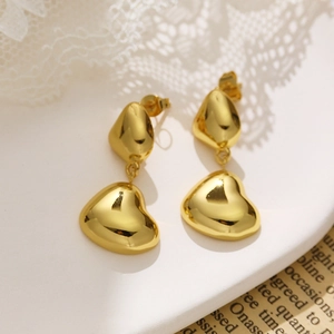 Polished gold double-layer heart earrings on white lace and aesthetic magazine background