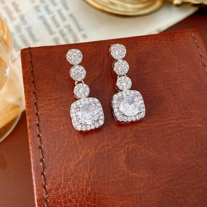 Detail showing elegant silver earrings with square zircon stones on brown leather base