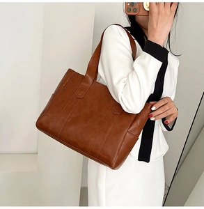 Brown leather tote bag held by a model wearing a white outfit against a clean background