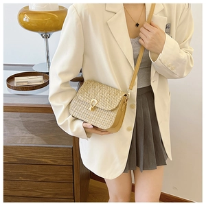 Detail of straw woven crossbody bag with gold U-shaped buckle and leather side panels