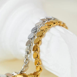 Detailed macro view of gold and silver leaf-shaped scale chain bracelets on white stone