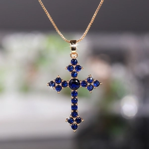 Detail of a gold box chain necklace with a cross pendant set in blue cubic zirconia