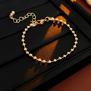 Detailed view of a golden beaded bracelet with lobster clasp on a black jewelry display