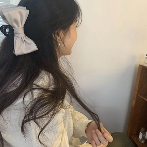 Detail of elegant beige satin bow hair claw clip styled on long straight hair