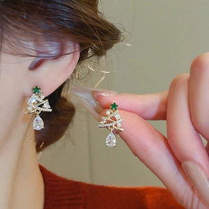 Close-up of golden Christmas tree earrings with sparkling zircons and a pearl drop