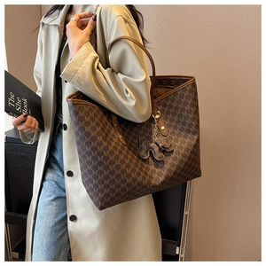 Close-up of large brown monogram tote bag with leather handles and dog charm accessory