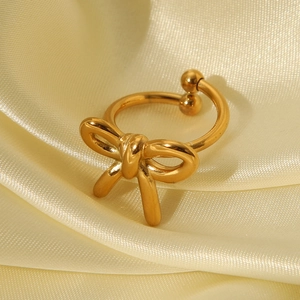 Detail of a golden bow-shaped open ring on soft yellow satin background with refined finish