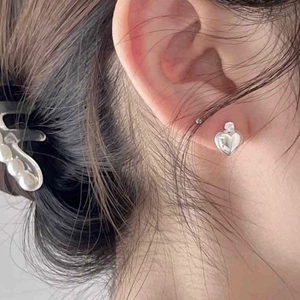 Close-up of heart-shaped silver stud earrings worn by a model with a soft natural look