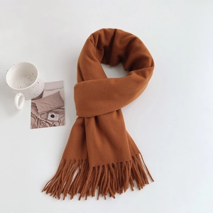 Flat lay of soft caramel cashmere-feel scarf with tassels next to a cozy coffee cup