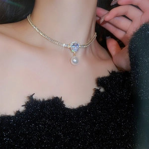 Macro detail of gold plated necklace with teardrop zircon and pearl on black background