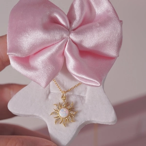 Close-up of golden sun pendant with white opal and zircon on a pink silk bow