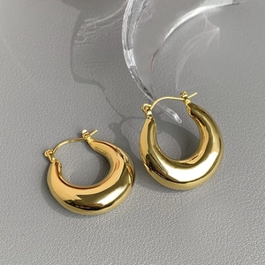 Detailed close-up of polished golden C-shaped hoop earrings on a grey textured surface