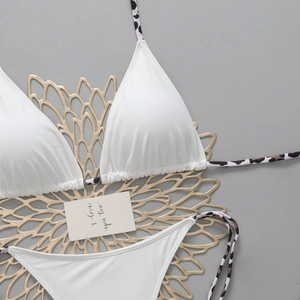 Detailed flat lay of white triangle bikini set with leopard print straps on a grey surface