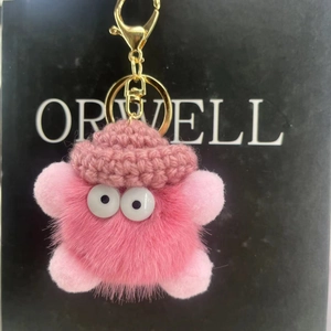 Close-up of pink fuzzy soot sprite keychain with crochet hat and golden metal clasp
