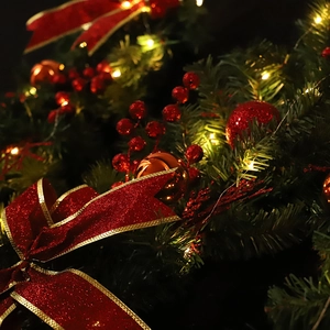 Lush green Christmas garland with red bows, ornaments, and warm LED fairy lights
