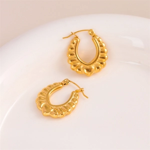 Textured gold heart earrings with embossed pattern on white ceramic tray