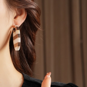 Close-up of C-shaped striped earrings with brown wood and cream resin textures