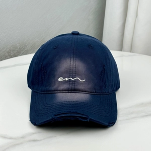 Detail of navy blue cotton baseball cap featuring worn distressed holes and em embroidery