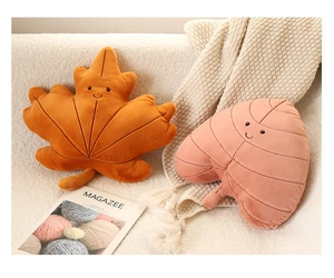 Detail of plush leaf pillows in orange and pink featuring cute embroidered smiley faces