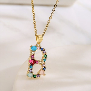 Gold letter B pendant necklace with multi-colored gemstones on minimalist stone surface