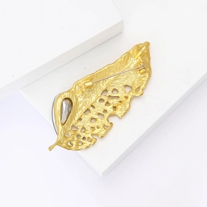 Detailed back view of golden feather brooch with safety pin clasp on a white platform