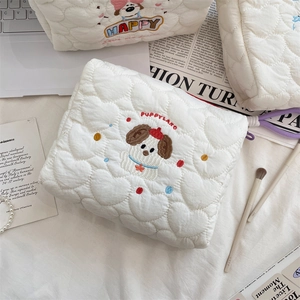 Detail of white quilted puppy makeup bag with embroidery and lifestyle makeup items