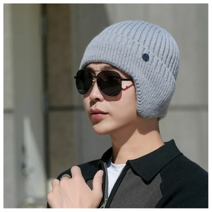 Detail of light gray knit trapper hat with soft ribbed texture and metal logo