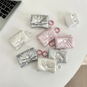 Three puffy bow-knot headphone pouches in silver, pink, and white on a minimalist desk