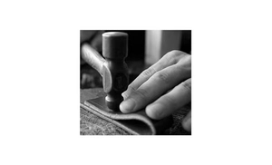 Close-up of artisan handcrafting textured PU leather belt with professional tools