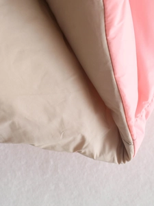 Detailweergave van roze buitenstof met beige binnenvoering op een gewatteerde vest
