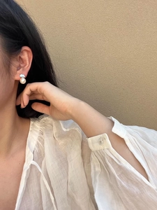 Close-up of elegant French style curved pearl earrings on model with white chiffon shirt