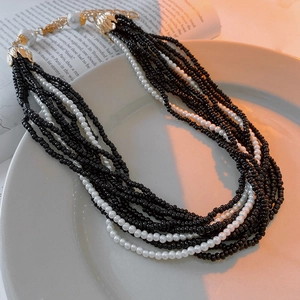Detail of multi-layer faux pearl necklace with gold leaf clasp on white ceramic plate