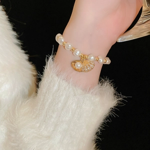 Detail of beaded pearl bracelet with gold shell charm worn over a white sweater