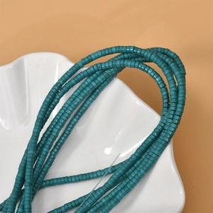 Detailed view of turquoise 2x4mm flat cylindrical beads on a white shell tray