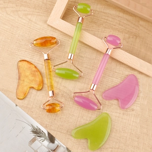 Close-up of three color resin facial rollers and heart-shaped gua sha tools on wood background