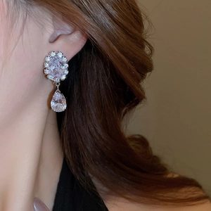Close-up of sparkling teardrop zircon drop earrings worn on ear with silver base