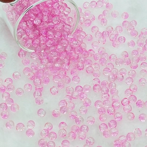 Macro shot of 6mm pink crackle glass beads pouring from a glass jar onto a soft white rug