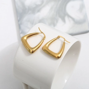 Close-up of gold water drop earrings with U-shaped flat hoop design on a ceramic cup