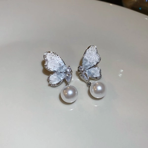 Macro view of butterfly earrings with crystal pavé wings and dangling white pearl charms