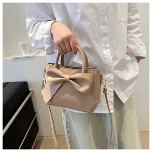 Detail of elegant beige bucket bag featuring a large bow and gold-tone hardware